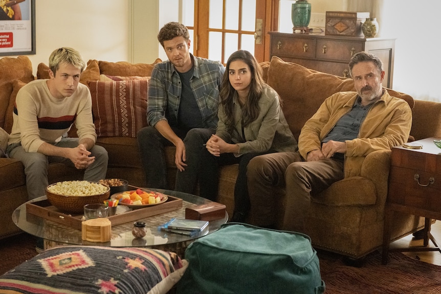 Three sombre-looking young people and a middle-aged man sit on a lounge looking up expectantly at someone out of frame