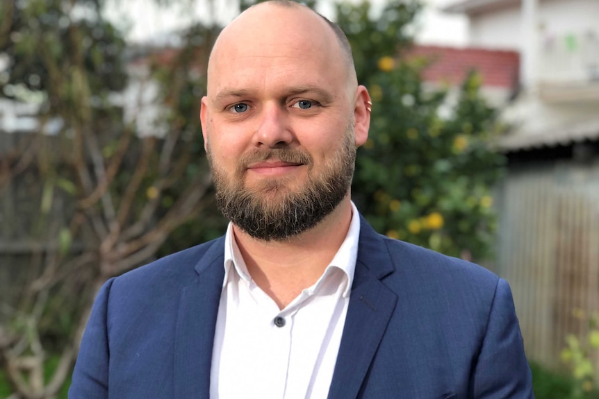 A portrait of Chris Maylea wearing a navy blue suit and looking at the camera.