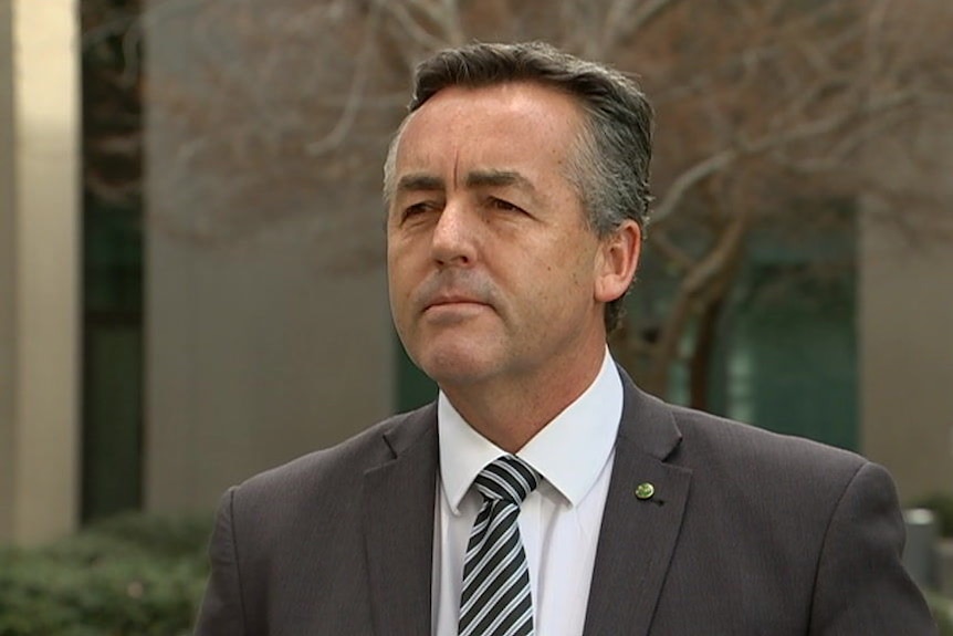 A man with salt and pepper hair, wearing a dark suit, in a courtyard.