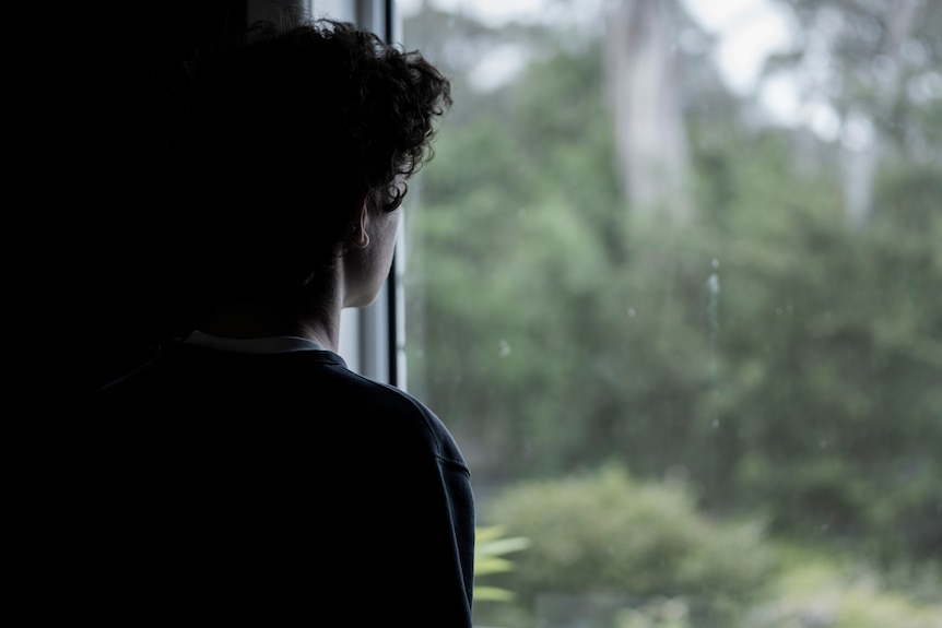 A teenage boy looks out a window.