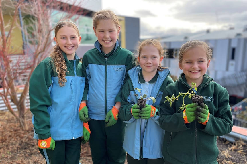 Students at St Mary's College in Hobart smile as they hold plants grown in their garden.