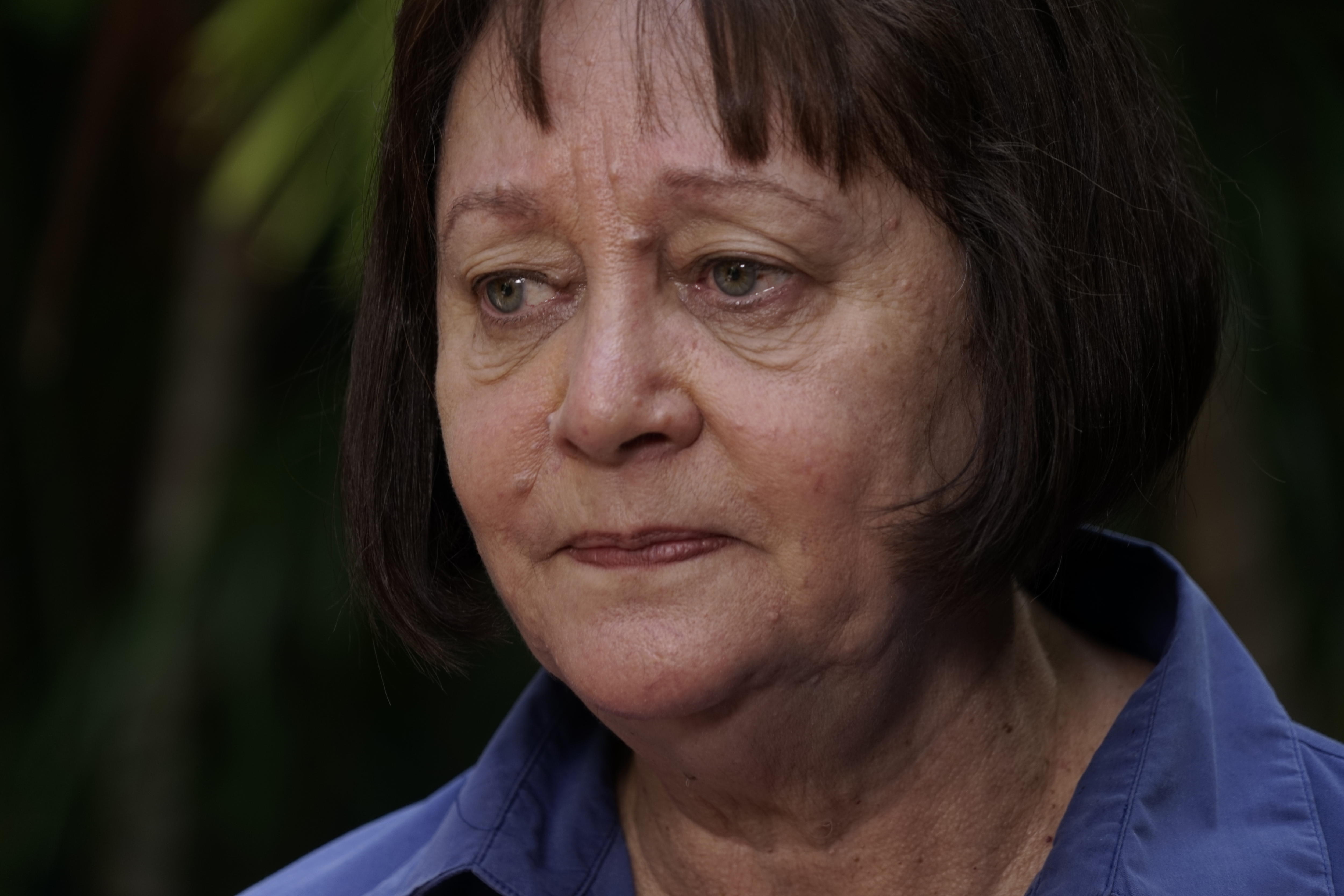 A photo of a woman wearing a blue shirt looking seriously off-camera. She has short, dark hair.
