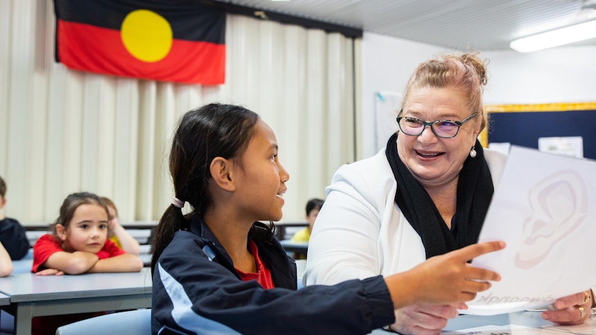 Education Minister Sue Ellery sitting with a child with an Aboriginal flag in the background.