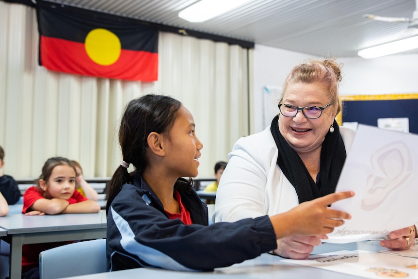 Education Minister Sue Ellery sitting with a child with an Aboriginal flag in the background.