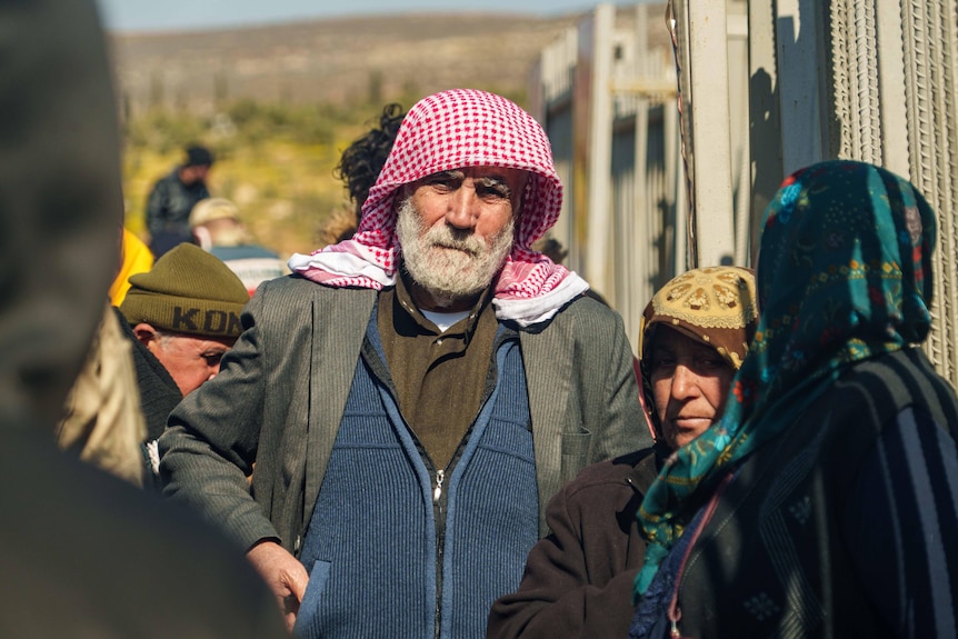 A man wears a checkered scarf while standing surrounded by people.