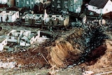 An aerial view of a Scottish street. Houses are in ruins and a crater runs through the middle of the street.
