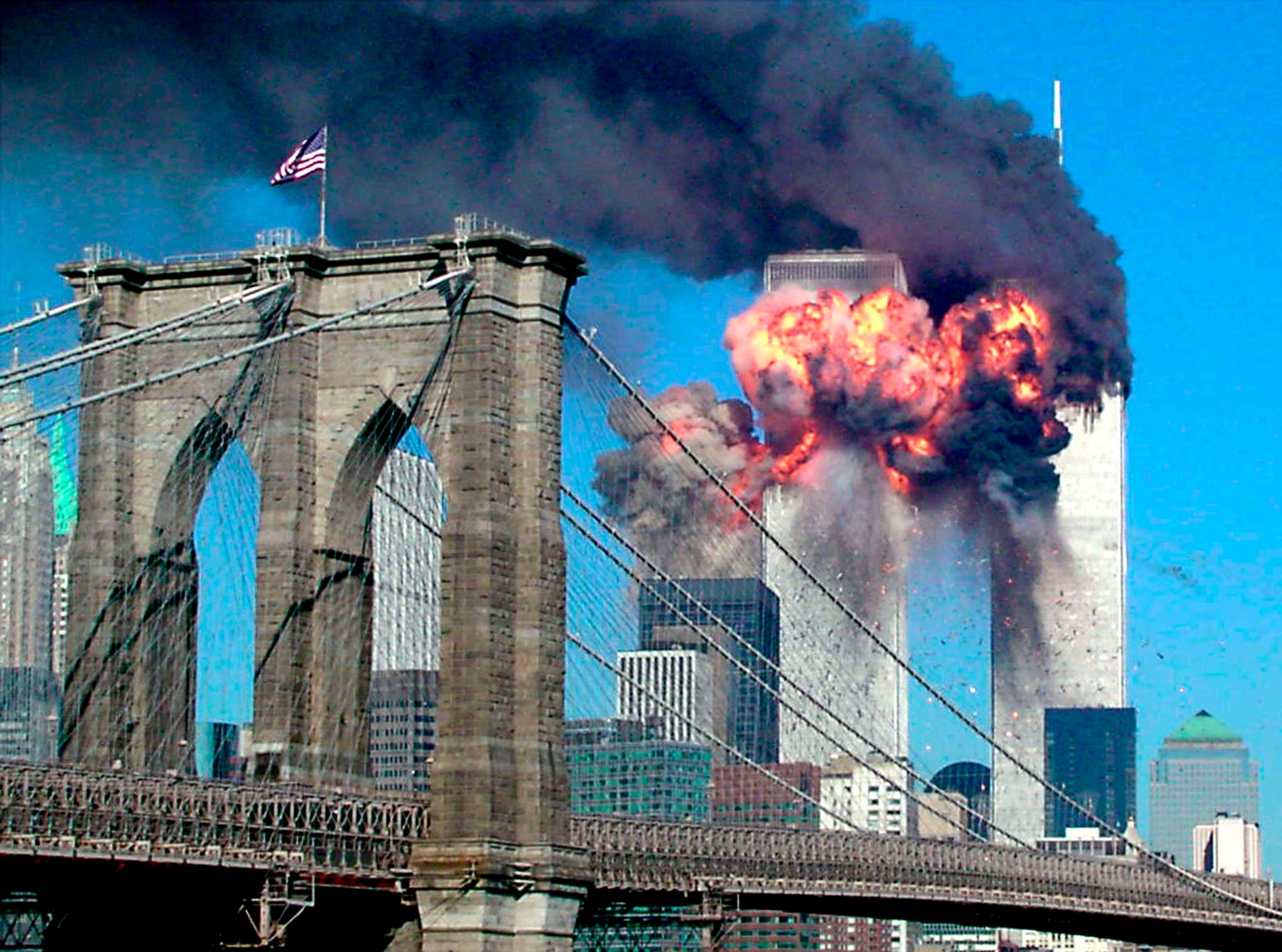 Two silver towers are engulfed in flames and smoke, with a bridge in the foreground