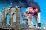 Two silver towers are engulfed in flames and smoke, with a bridge in the foreground