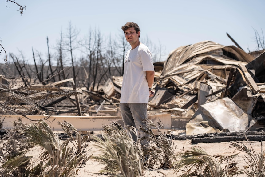 A man in a white t-shirt standing in a fiery wreckage