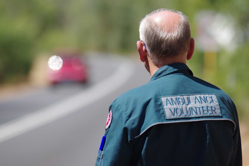 Volunteer ambulance officer in uniform, from behind, looks down a highway.