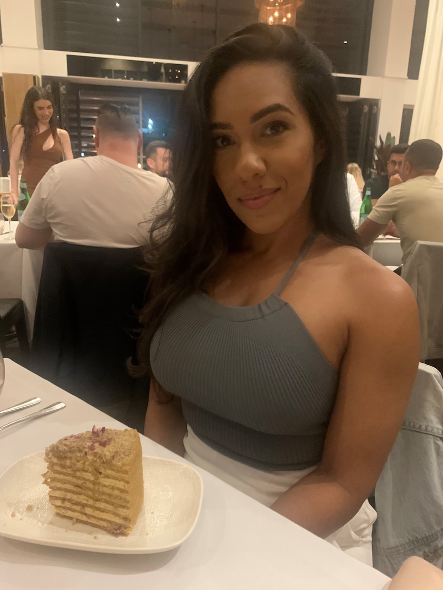Tahnee is wearing an olive green halter neck top sitting at a restaurant table in front of a slice of her birthday cake.