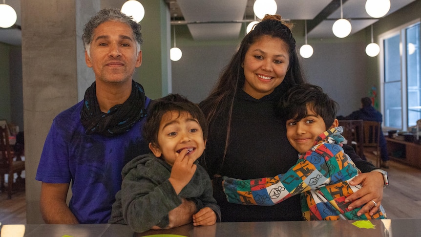 A family of dad, mum and two young kids smiles while embracing.