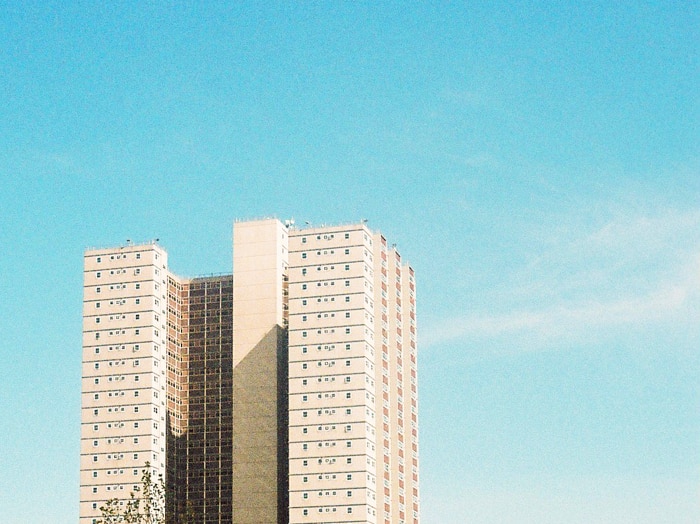 On a bright blue day, you view a multi-storey brutalist public housing tower in the distance.