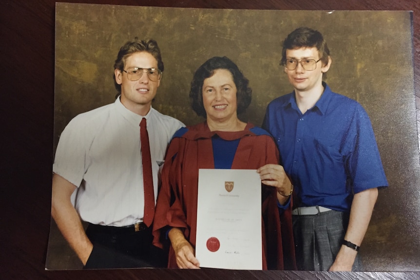 Michelle holds up university certificate with her two sons on either side