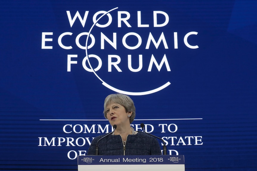 British Prime Minister Theresa May delivers a speech against a backdrop with the worlds 'World Economic Forum'.