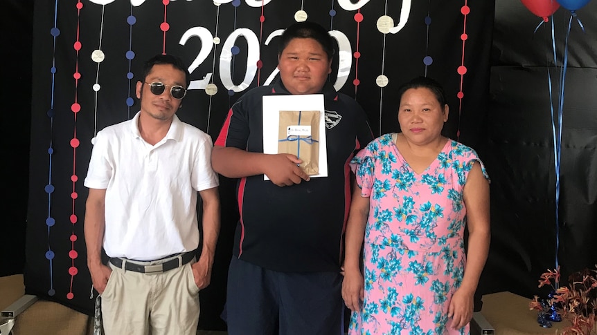 An Asian boy stands proudly between his parents. 