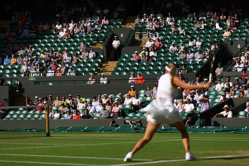 A tennis player out of focus in front of a mostly empty stadium. 