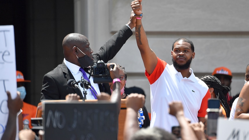 Two men are pictured during a rally, a suited man is holding up another man's hand. 