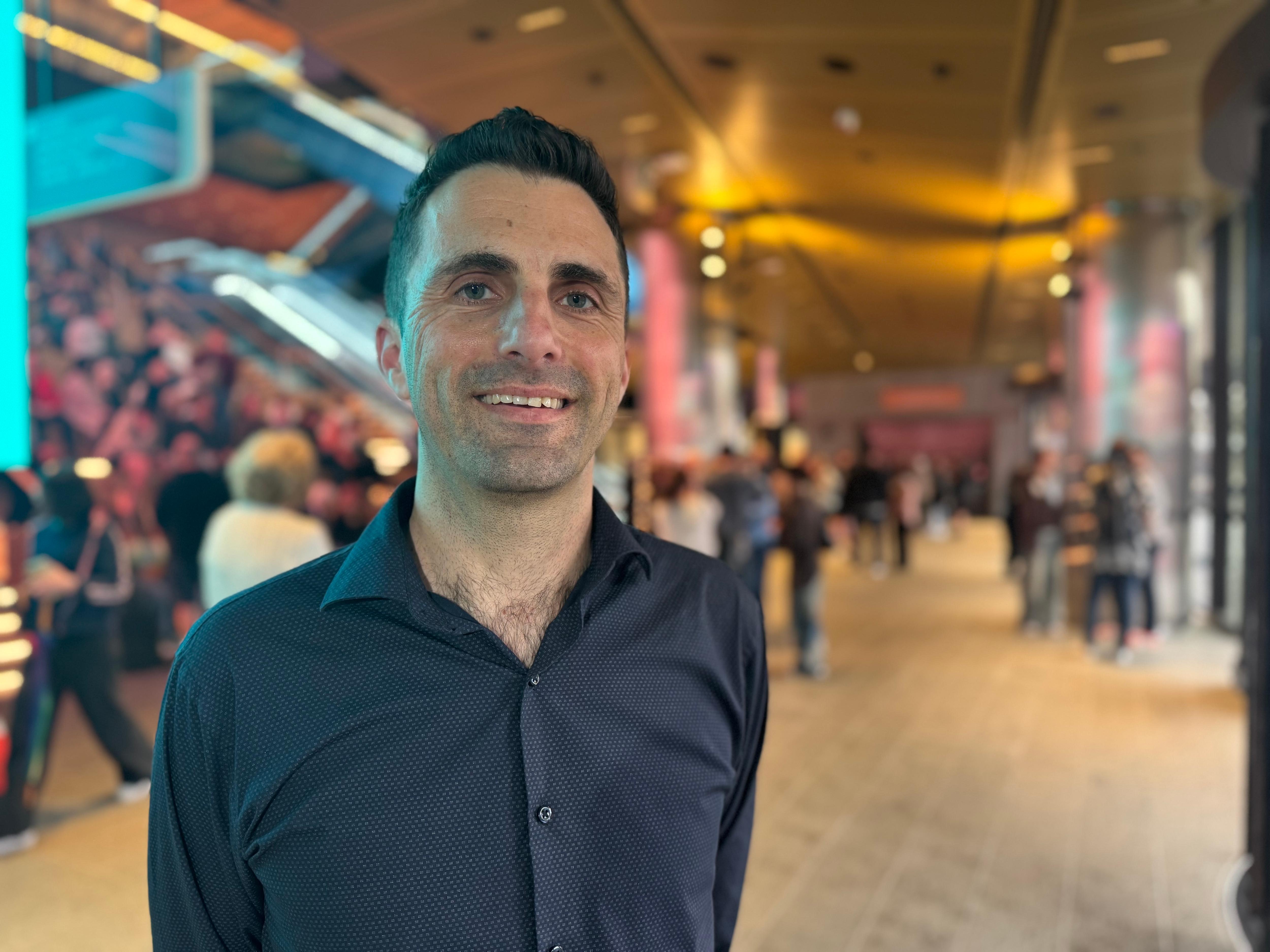 A man wearing a dark blue shirt smiles. 