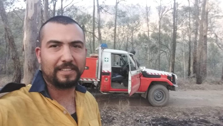 A firefighter in uniform takes a photo in front of his truck