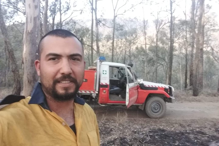 A firefighter in uniform takes a photo in front of his truck