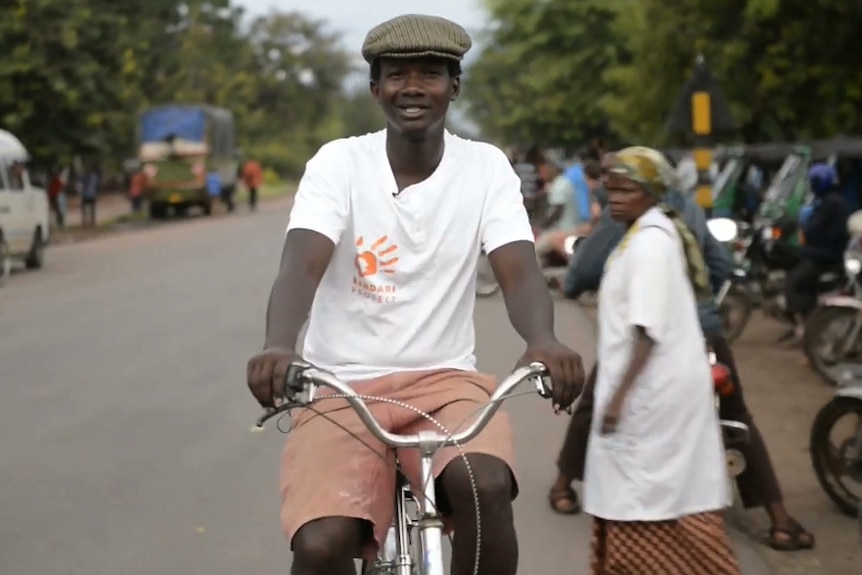 An African man in a white t-shirt rides a bike on a road in Tanzania.