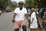 An African man in a white t-shirt rides a bike on a road in Tanzania.
