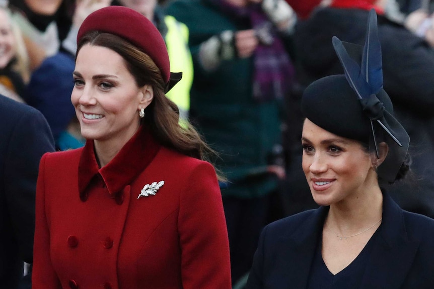 Kate Middleton, left, enters church wearing a matching red coat and hat along with Meghan Markle, wearing a navy coat and hat.