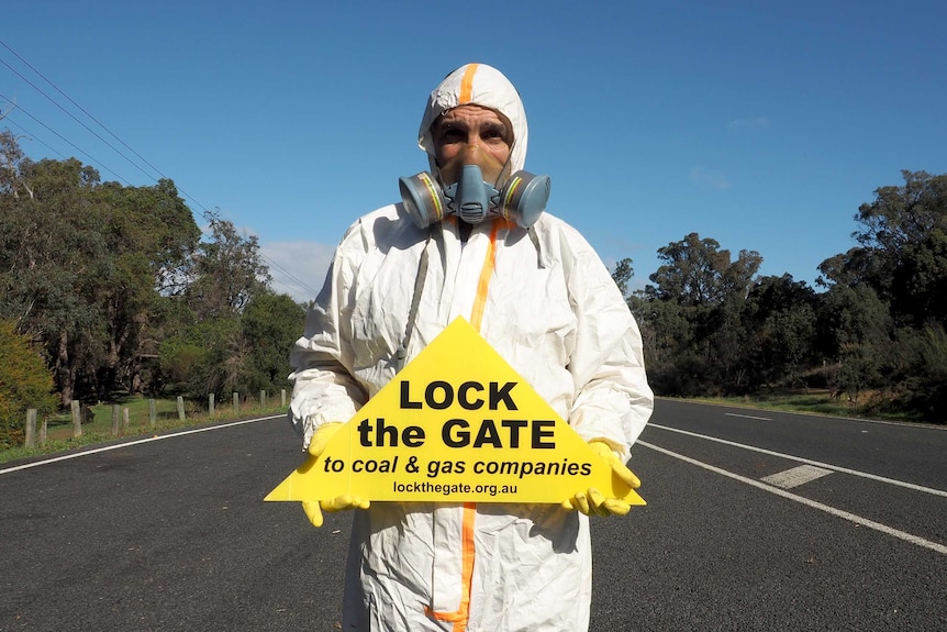 An unidentified man stands in road holding no fracking sign.