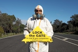 An unidentified man stands in road holding no fracking sign.