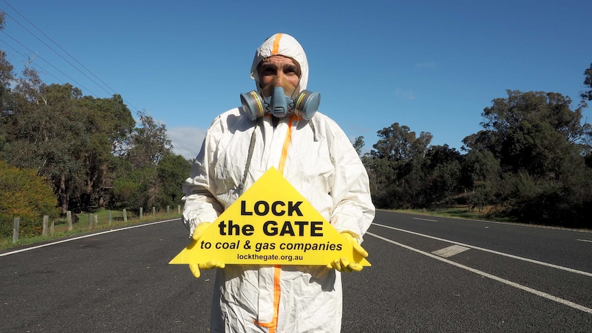 An unidentified man stands in road holding no fracking sign.