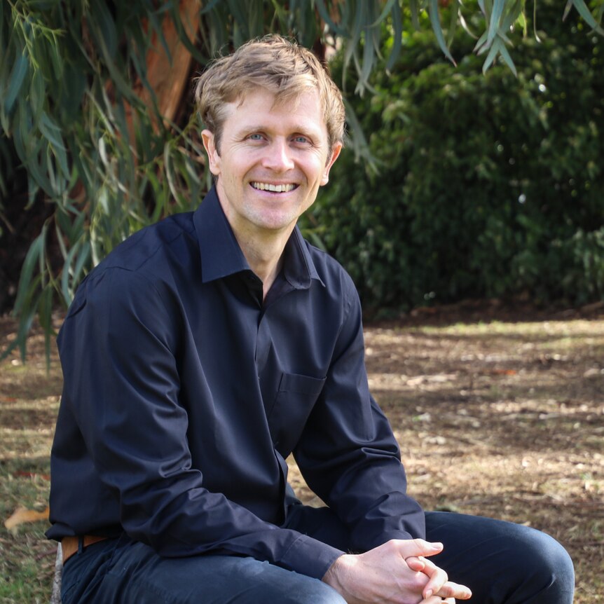 Andre Leslie in a park, with gum trees in the background.