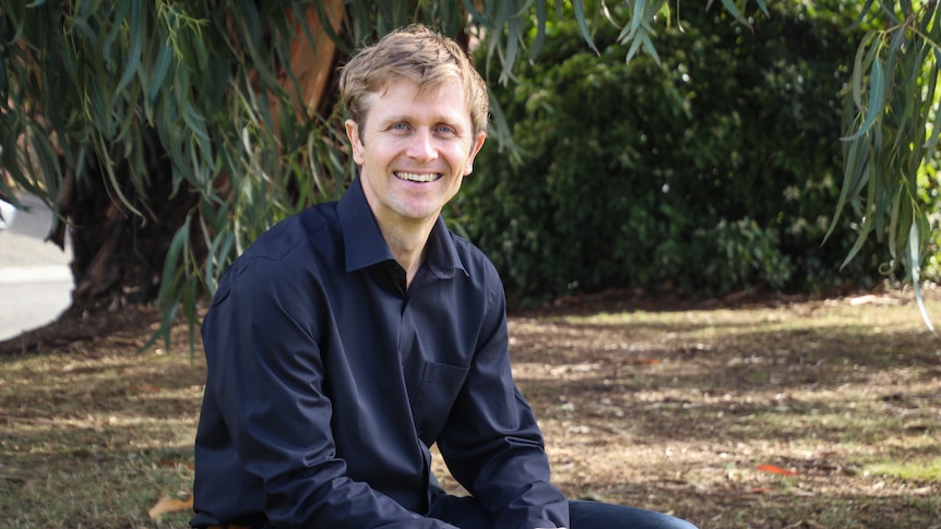 Andre Leslie in a park, with gum trees in the background.