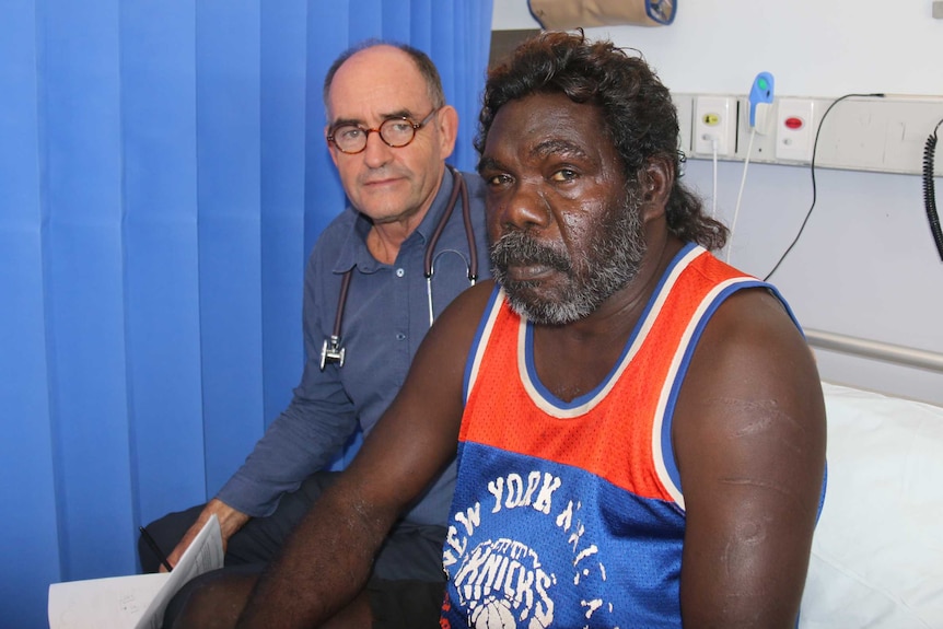 Two men sit together on a hospital bed.