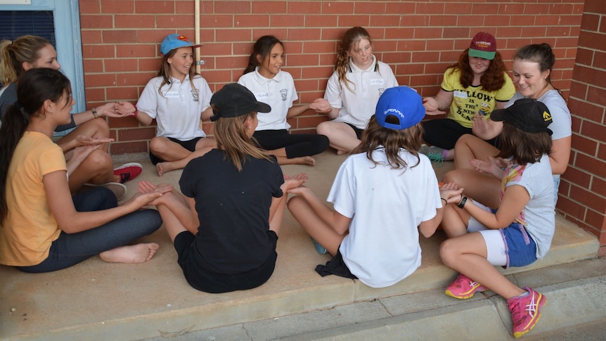 Eight students and two mentors sit in a circle with legs crossed, holding hands 