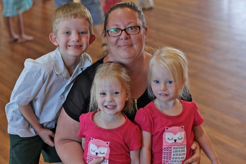 Townsville woman Tracey Ross squats on the ground with her children Mitchell, Kaitlin and Chloe.