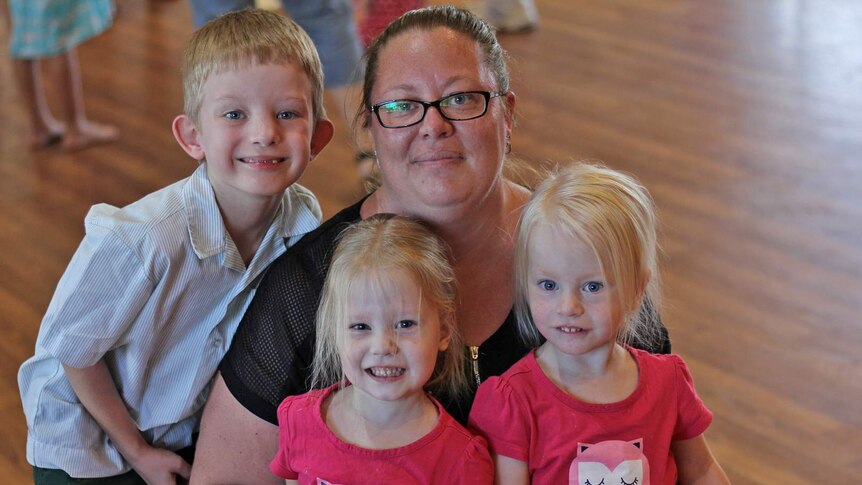 Townsville woman Tracey Ross squats on the ground with her children Mitchell, Kaitlin and Chloe.