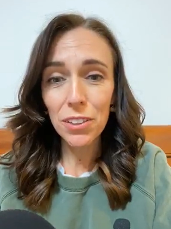 Jacinda Ardern mid-speech, wearing a green jumper and sitting against an orange couch