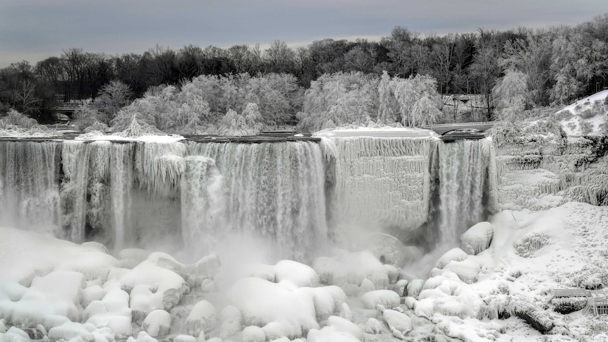 A waterfall continues to flow white the areas surrounding it frozen over with snow and ice.