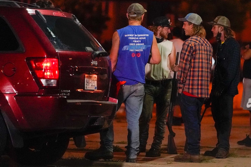 Four men stand near a car holding guns during protests in Kenosha.