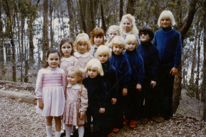 Two lines of children, girls on one side and boys on the other, stand wearing matching outfits. 