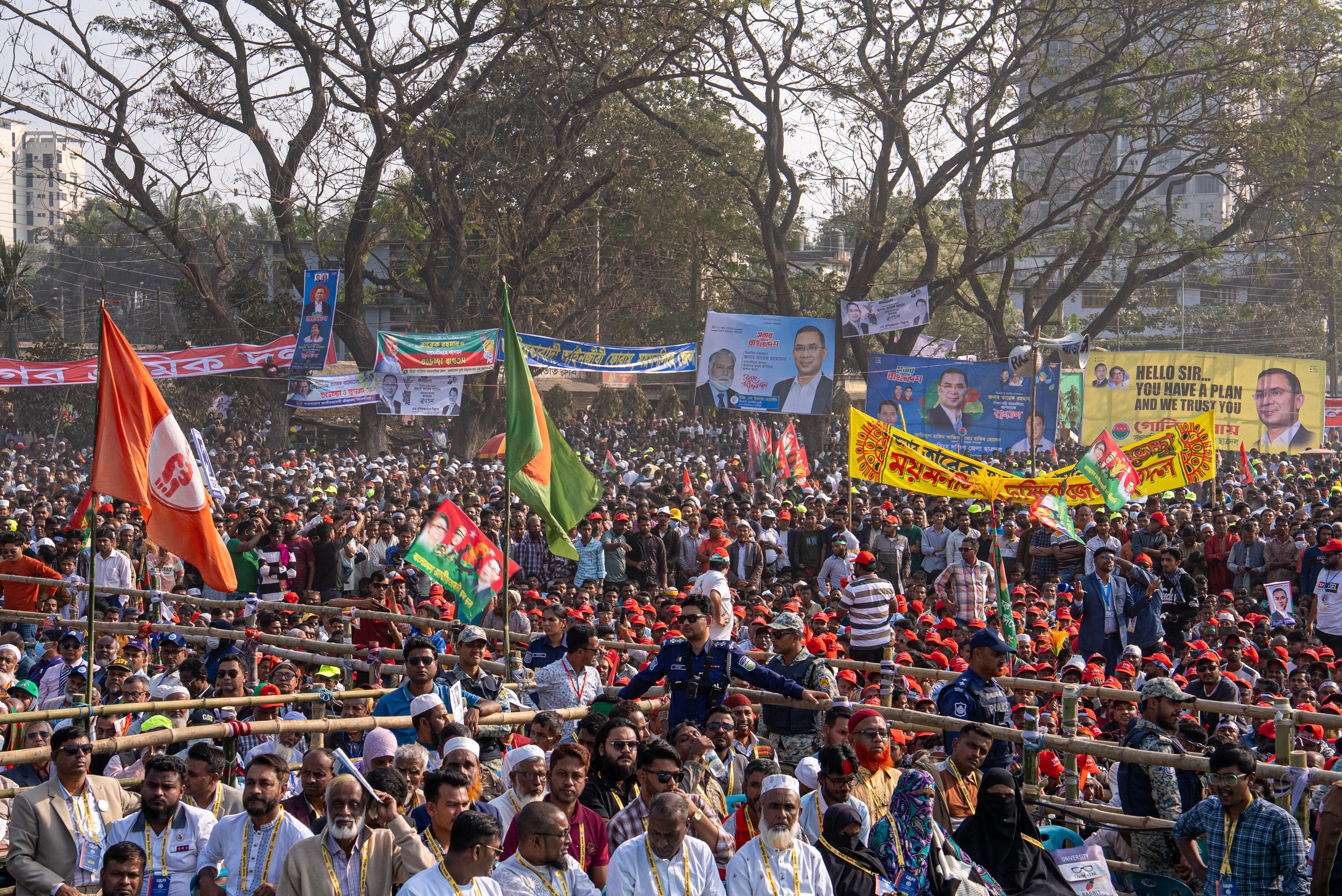 A crowd of people holding flags and posters in support of candidates stand in a street.