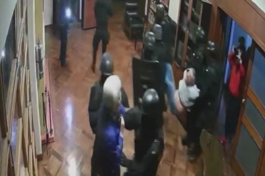 CCTV vision of security forces inside a hallway of a building apprehending a person.