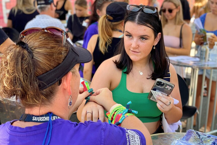 A young woman in a crowd gets a wristband put on by an event official.