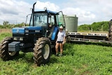 Robyn Lethbridge standing next to a tractor, truck and water tank in a green paddock.