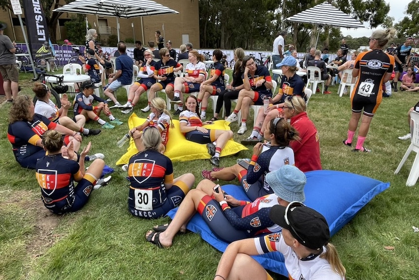 Two dozen people wearing cycling clothes sitting on beanbags after a race