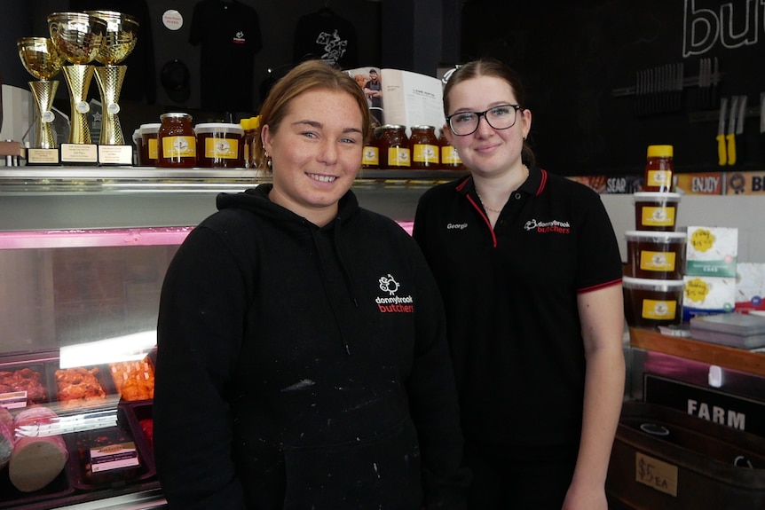 Two young women in black uniforms stand inside a butcher shop