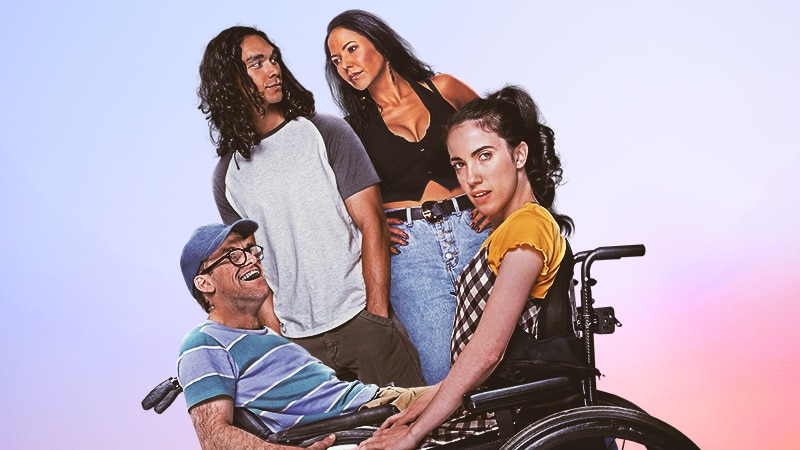 A man wearing a cap and a woman in a yellow tshirt are in a wheelchair as another man and a woman stand in the background