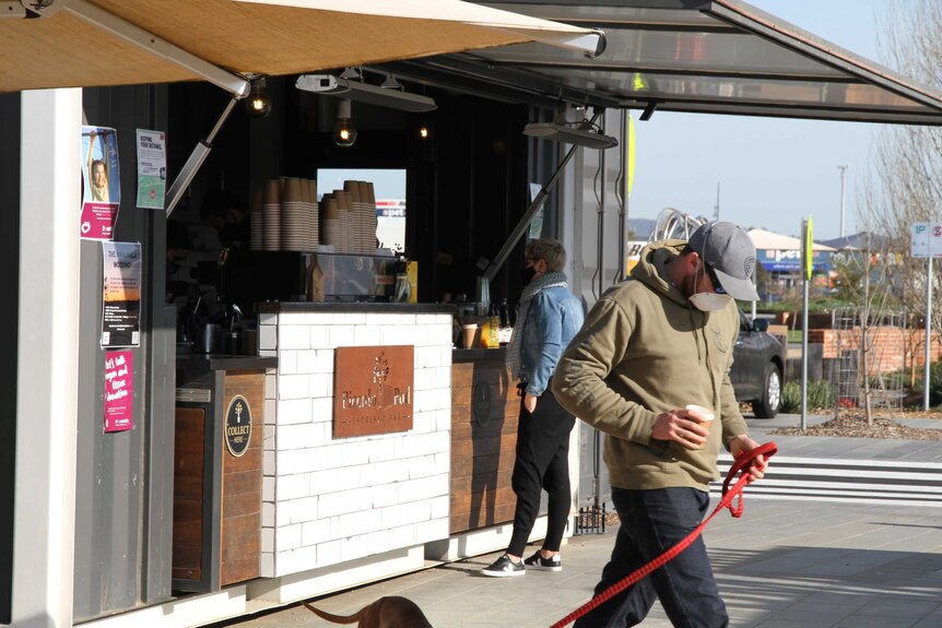 A man clad in a face mask orders a coffee from a takeaway van as another man walks away.