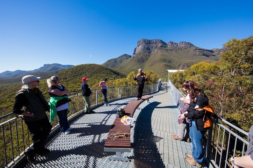 A indigenous tour guide stands with a tour group in front of a mountain